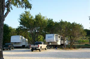Fifth-wheel trailers and pickup trucks on gravel sites under the trees